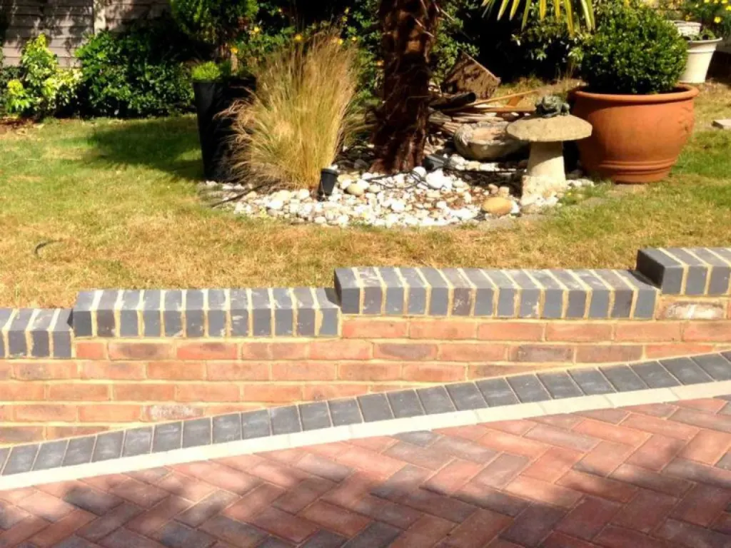 Landscaping contractors in Enfield brick garden wall installation with a landscaped lawn and plant pots in the background
