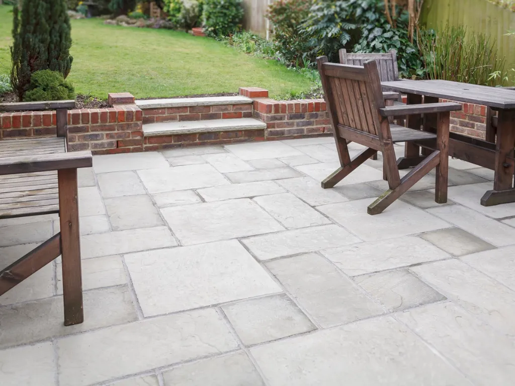 Paving contractors in Hertfordshire laying natural stone patio slabs with a small brick wall leading to a lawn