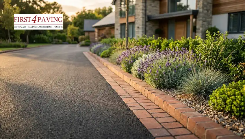 An asphalt driveway with a neat brick paver border runs alongside lush flower beds filled with purple lavender