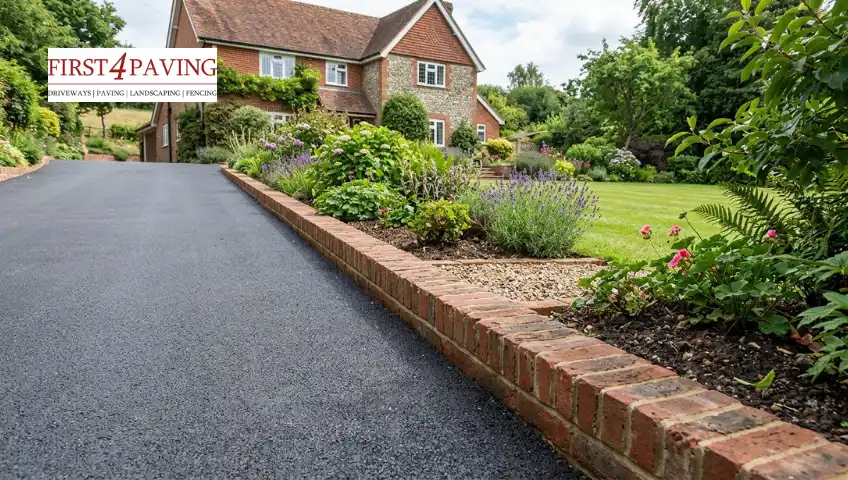 A smooth asphalt driveway with a low brick retaining wall leads up to a large brick and stone country house